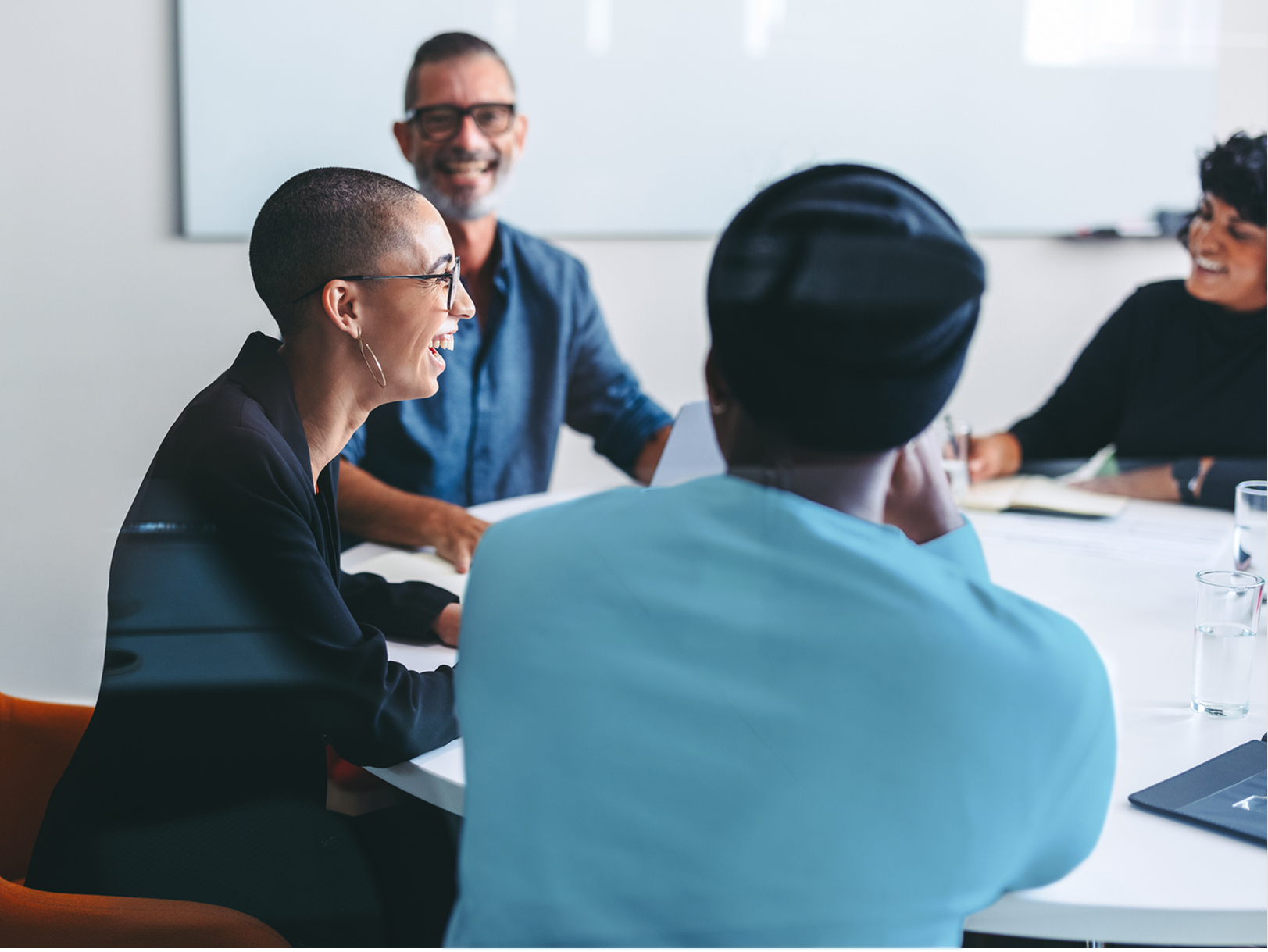 Profile of smiling woman at table with three other people in a meeting setting.